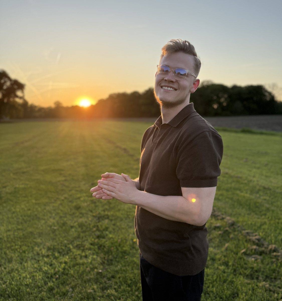 Niklas lächelt auf einer Wiese im Licht der tief stehenden Sonne.