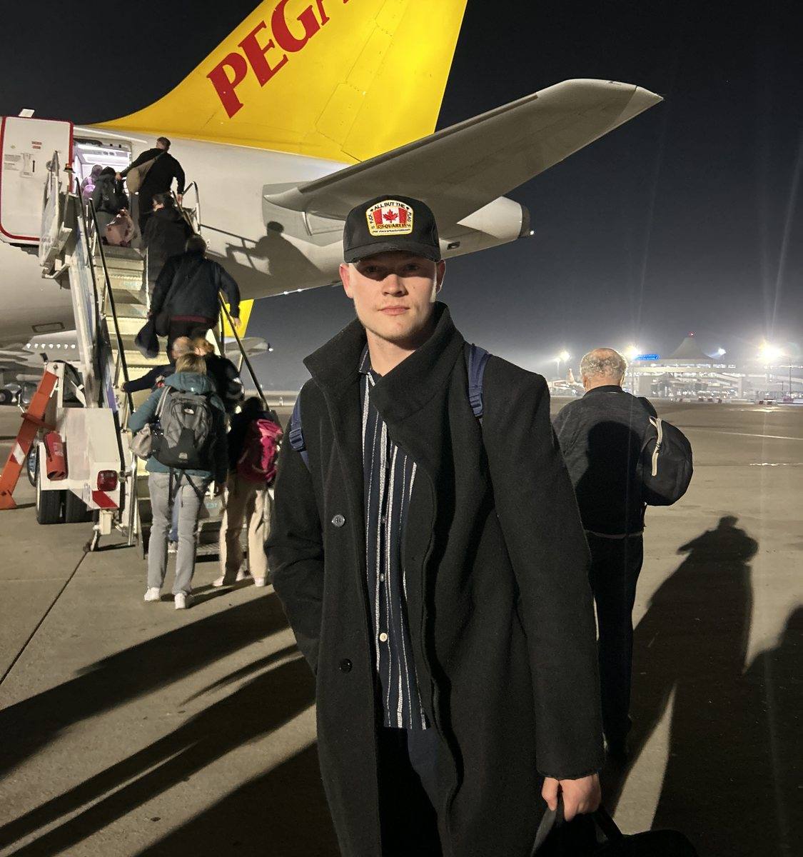 Niklas steht nachts auf dem Vorfeld vor einem Flugzeug, im Hintergrund steigen Reisende ein.