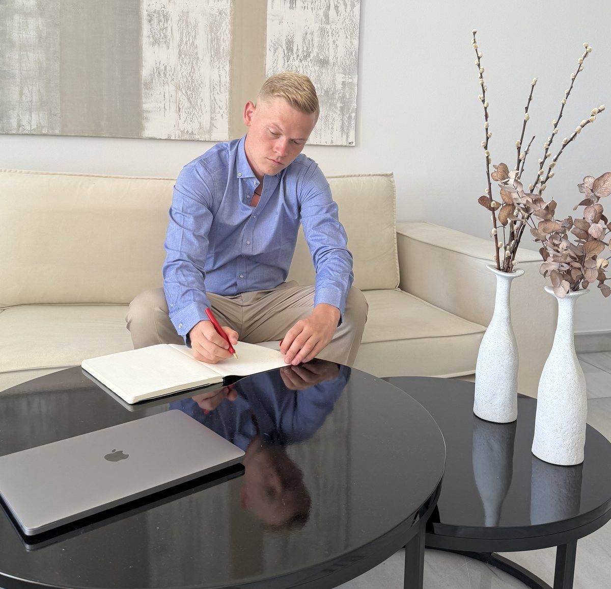 Niklas unterschreibt an einem Couchtisch ein Dokument, daneben ein Laptop.